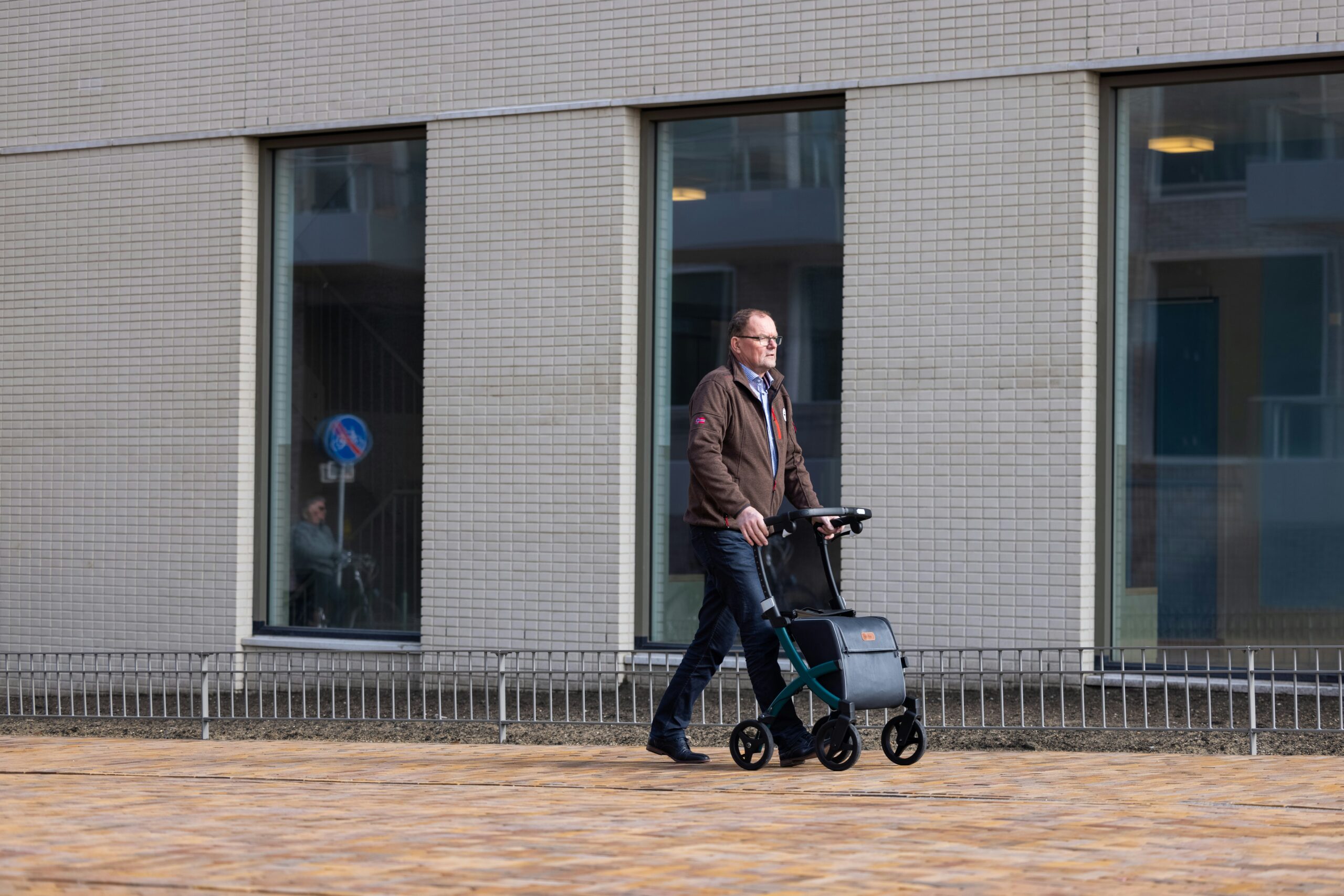 een man duwt een rollator op de stoep